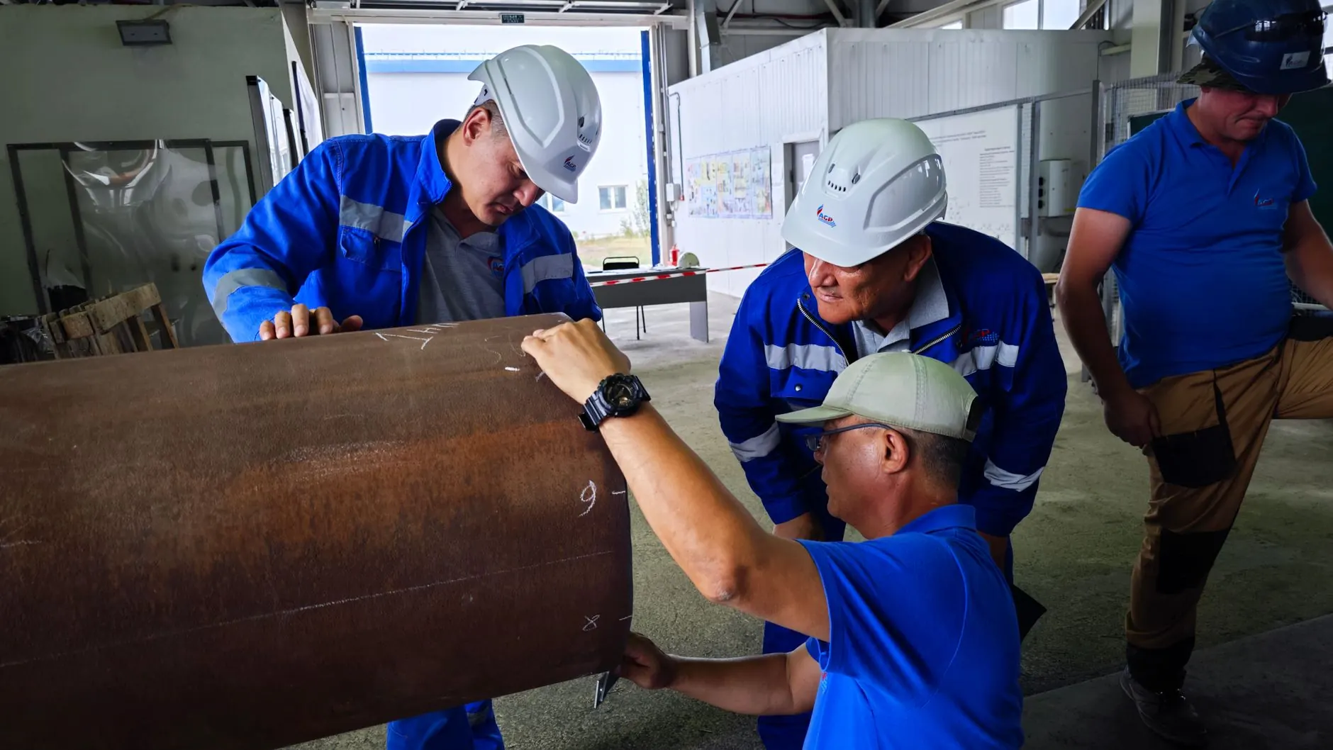 Equipe de operários de uniforme azul inspecionando uma grande tubulação