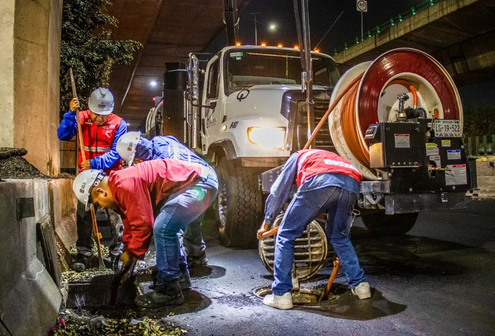 Equipe de desentupimento operando caminhão de limpeza de esgoto à noite em Lagoa Santa