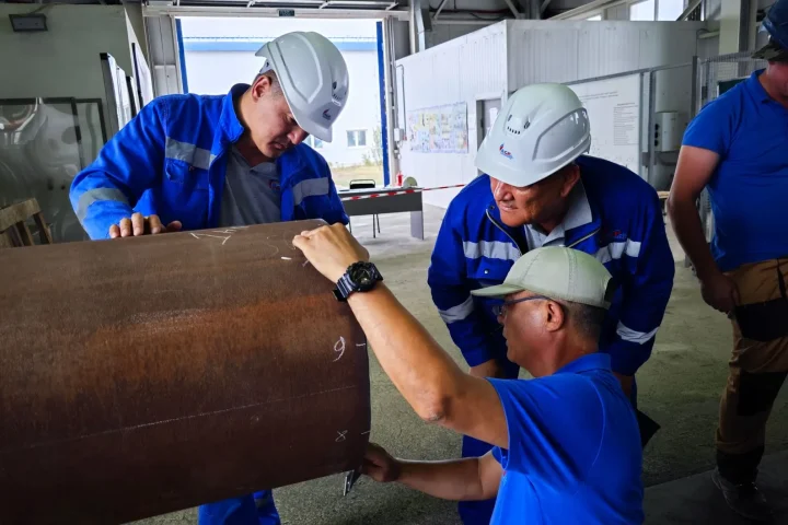 Equipe de operários de uniforme azul inspecionando uma grande tubulação
