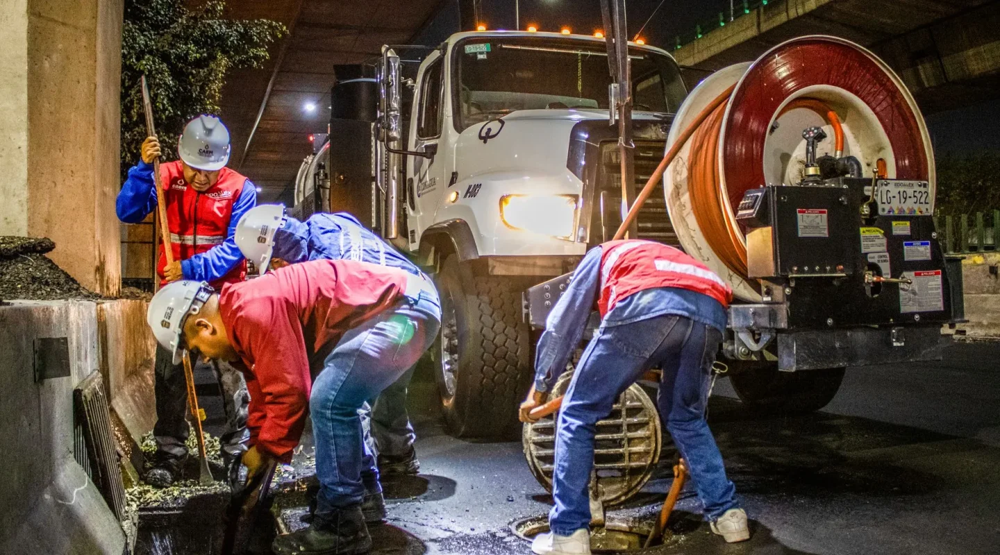 Equipe de desentupimento operando caminhão de limpeza de esgoto à noite