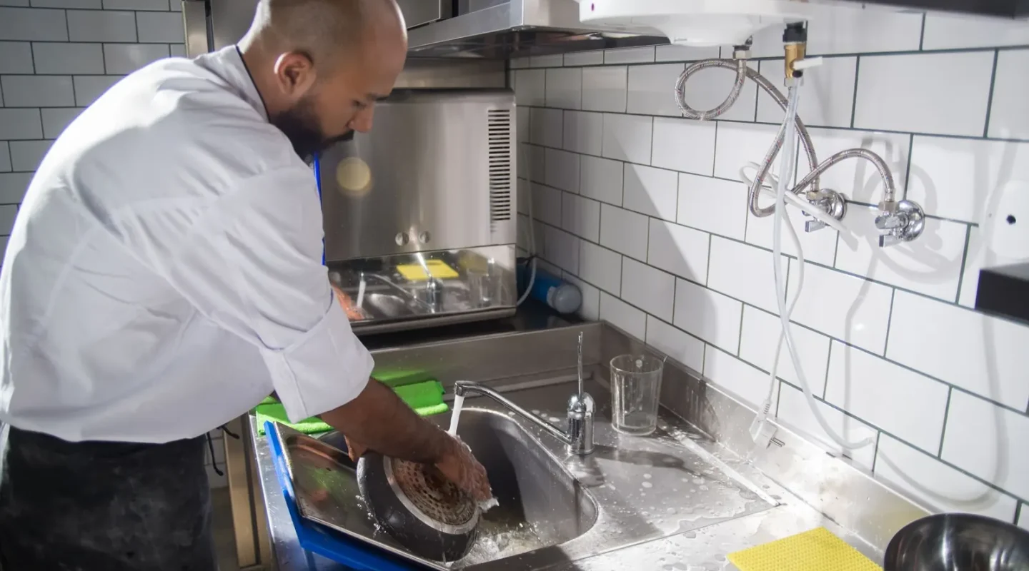 Cozinheiro lavando utensílios na pia de inox de uma cozinha profissional