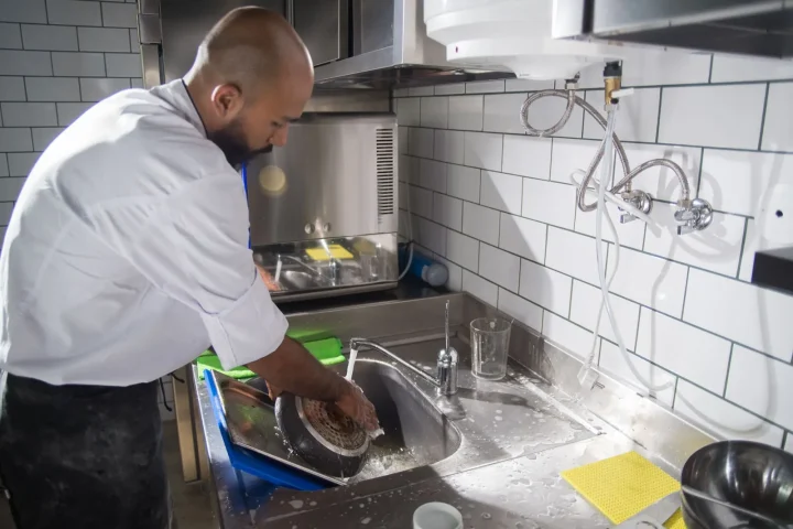 Cozinheiro lavando utensílios na pia de inox de uma cozinha profissional